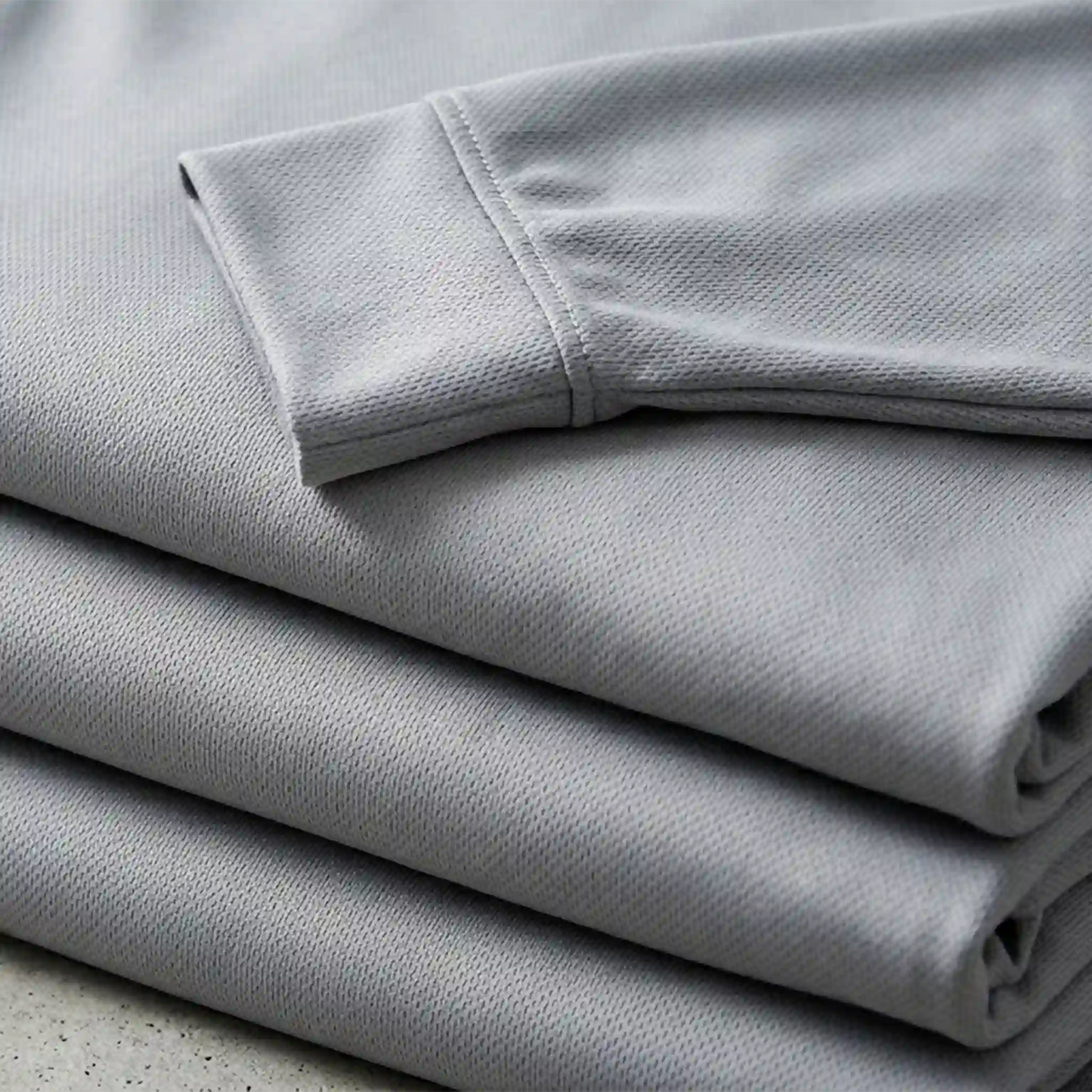 A stack of folded long-sleeve performance shirts showing high-quality fabric texture and durable collar construction - Made in Mount Pearl, NL.