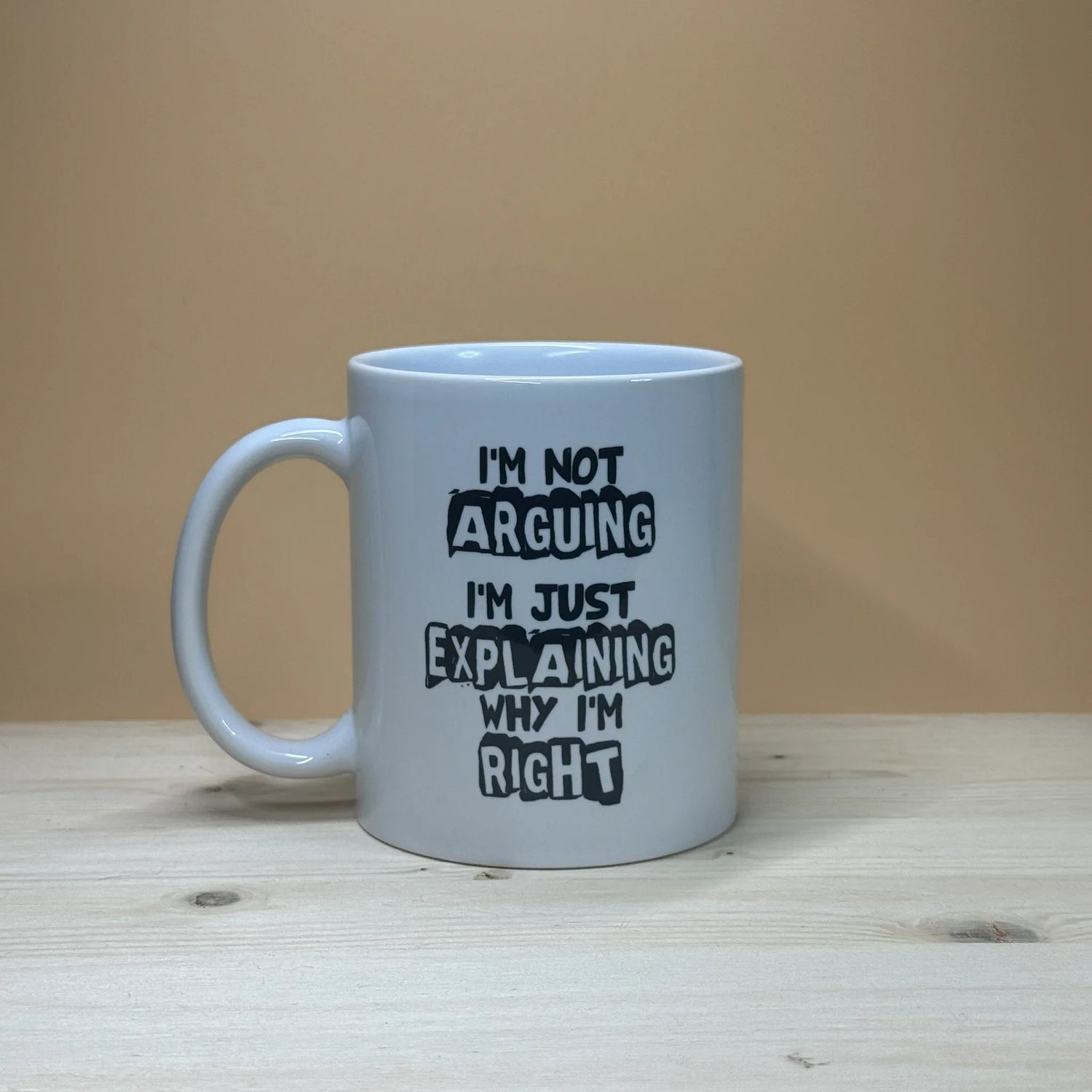 Coffee mug on a wooden surface with the saying: I'm Not Arguing, I'm Just Explaining Why I'm Right