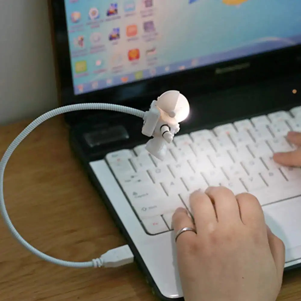A white Astronaut USB LED light with a flexible cord plugged into a laptop, illuminating the keyboard in a dark room.