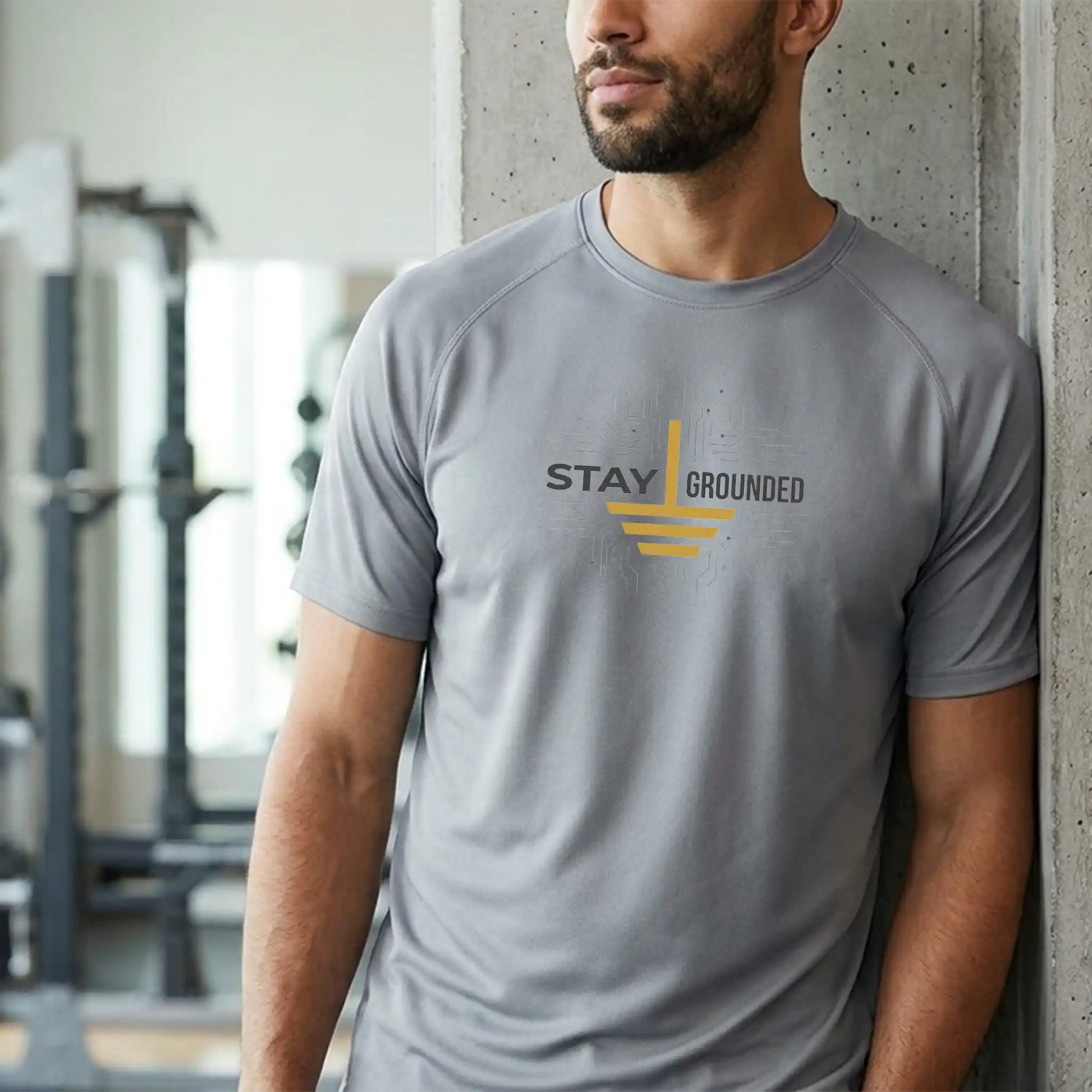 A fit male tradesperson wearing the short-sleeve 'Stay Grounded' performance tee in a modern gym setting, highlighting the moisture-wicking fabric and raglan sleeves.